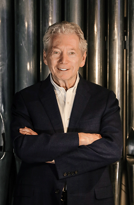 Dr. Gordon Turk standing in front of organ pipes in the Great Auditorium with his arms crossed.
